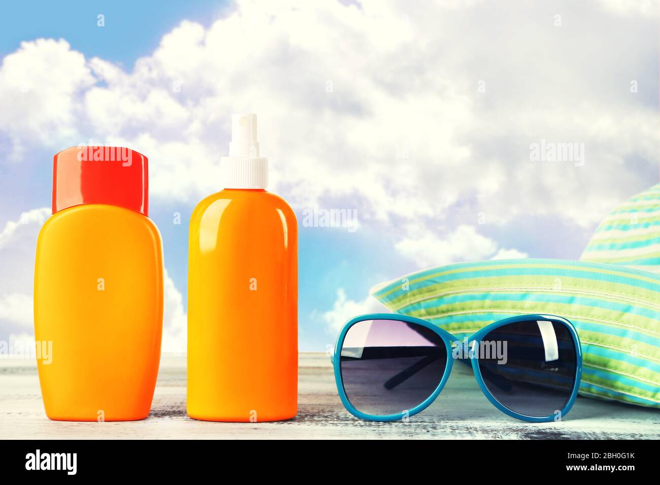 Bottles of suntan cream with sunglasses and hat on table isolated on