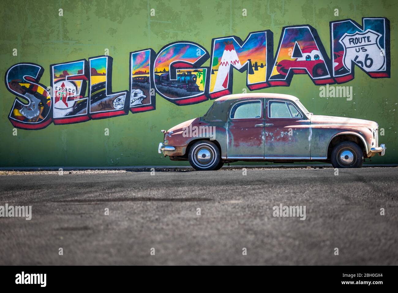 Close up of the Seligman logo painted on a green plaster wall, with a weathered red sedan car parked just below it Stock Photo