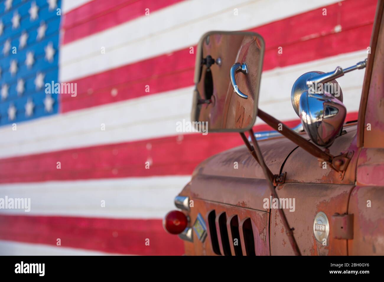 Close up of a an old and rusty red pickup truck parked against a brick wall painted with the american flag Stock Photo