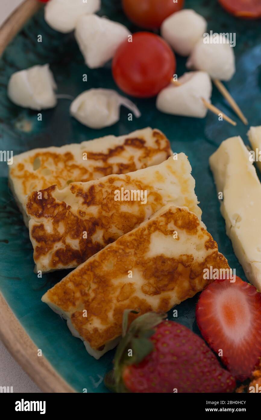 Vertical image of hellim cheese served on the platter with other cheese, tomatoes and strawberries. Stock Photo