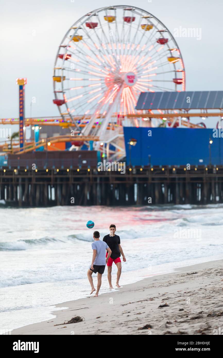 Two boys are playing with a soccer ball on the shore in front of the Santa Monica pier and its wonderwheel Stock Photo