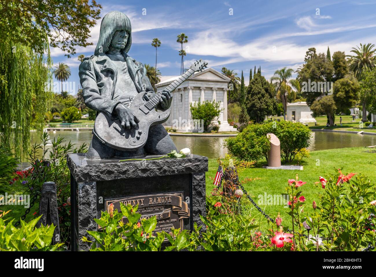 Close up Johnny Ramone bronze tombstone in Hollywood Forever, portraying him playing a guitar, with vegetation in the background Stock Photo