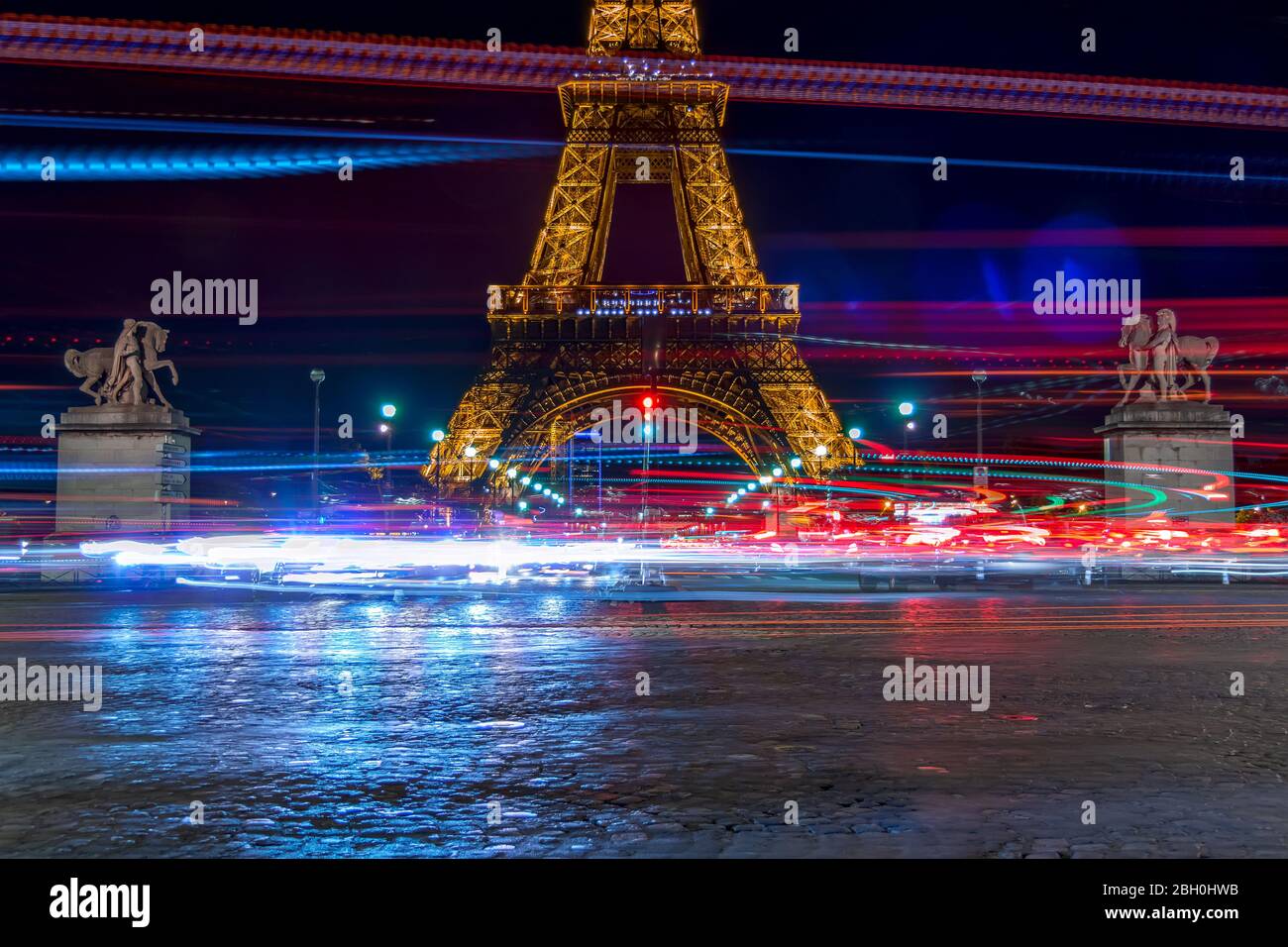 France. Night at the foot of the Eiffel Tower. Heavy traffic leaves lots of long exposure lights Stock Photo