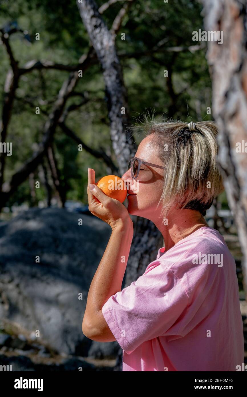 Adult woman holding orange in the palm and smelling it in the nature. Stock Photo