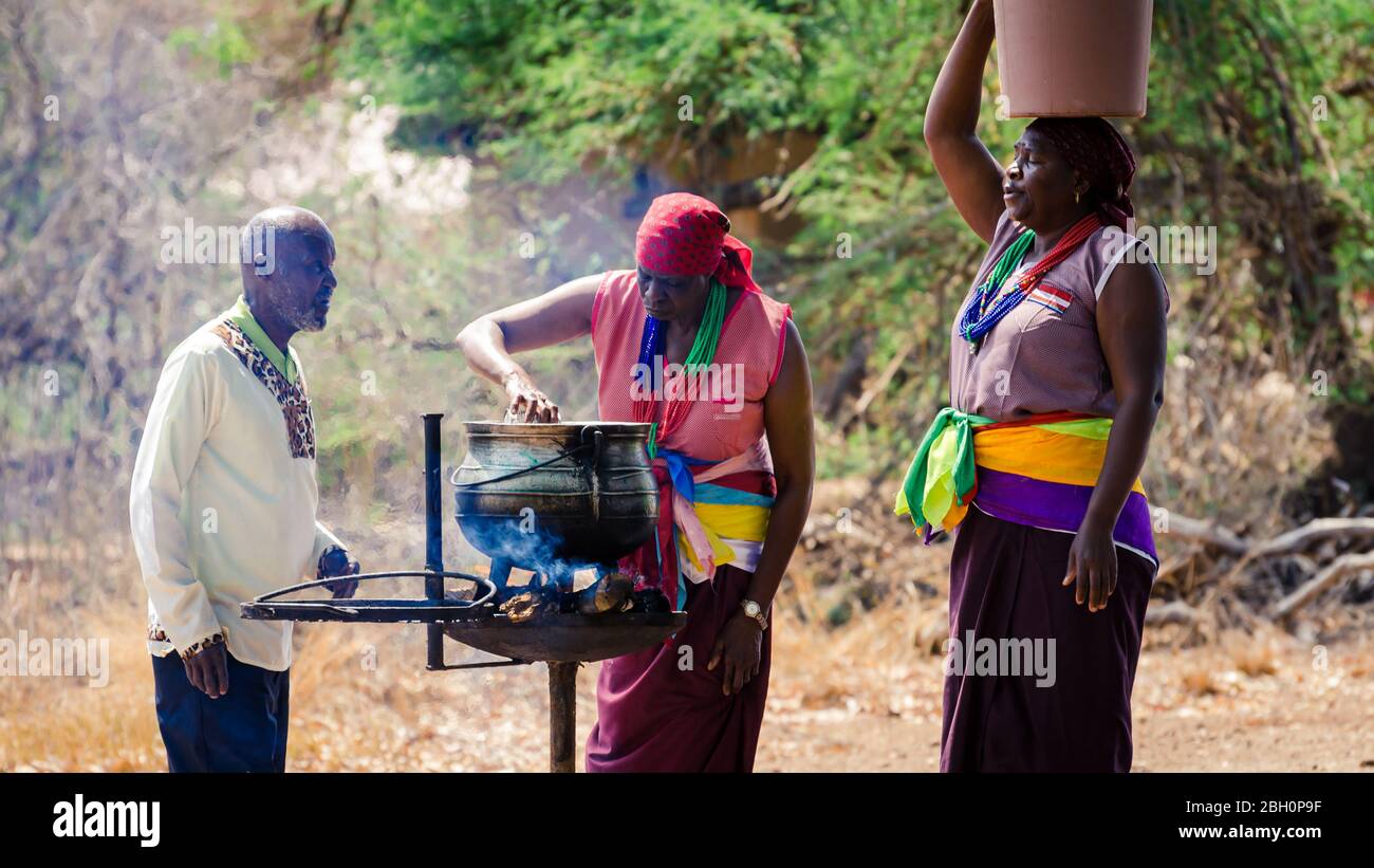 African ladies in traditional bright dresses making a soup in a large cauldron over hot charcoal braai  Kruger Safari Park South Africa Stock Photo