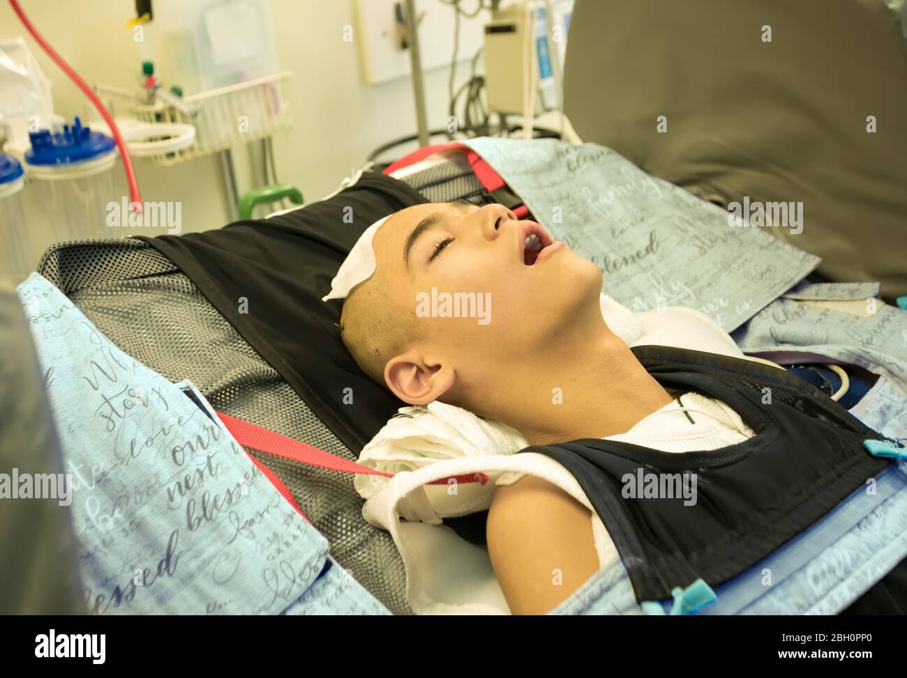 Young disabled teen boy lying in hospital bed unconscious after getting head or brain surgery Stock Photo