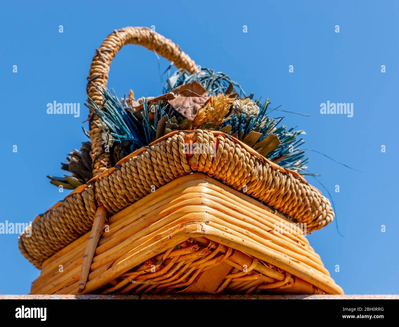 Bottom view of a nice wicker basket filled with a composition of dried plants and flowers against the blue sky of a sunny day Stock Photo