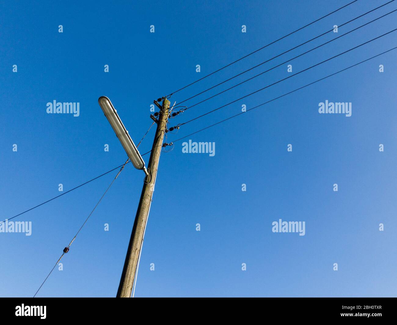 Street lamp and wooden telephone pole with cables and wires against clear blue sky in the countryside in Rhineland-Palatinate, Germany, Western Europe Stock Photo