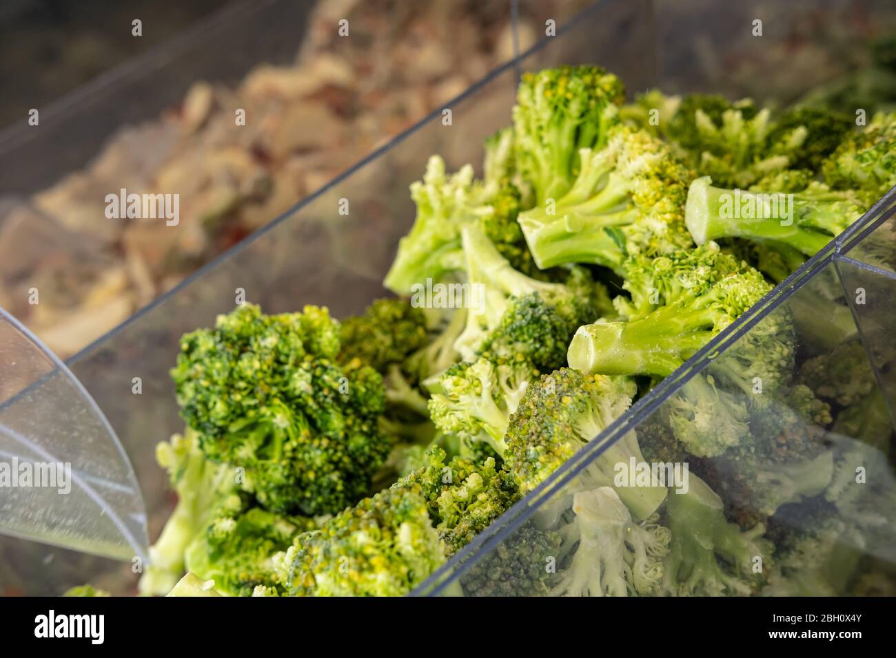 Frozen broccoli in a transparent container, on a counter in a store, on a blurred background