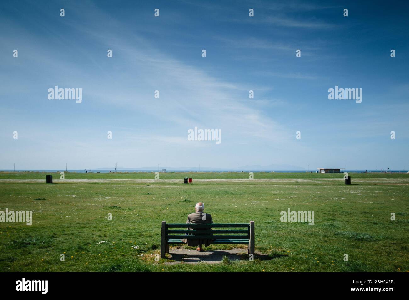 An elderly man sits alone on a bench at Ayr beach, during the Corona Virus pandemic lock down. Stock Photo