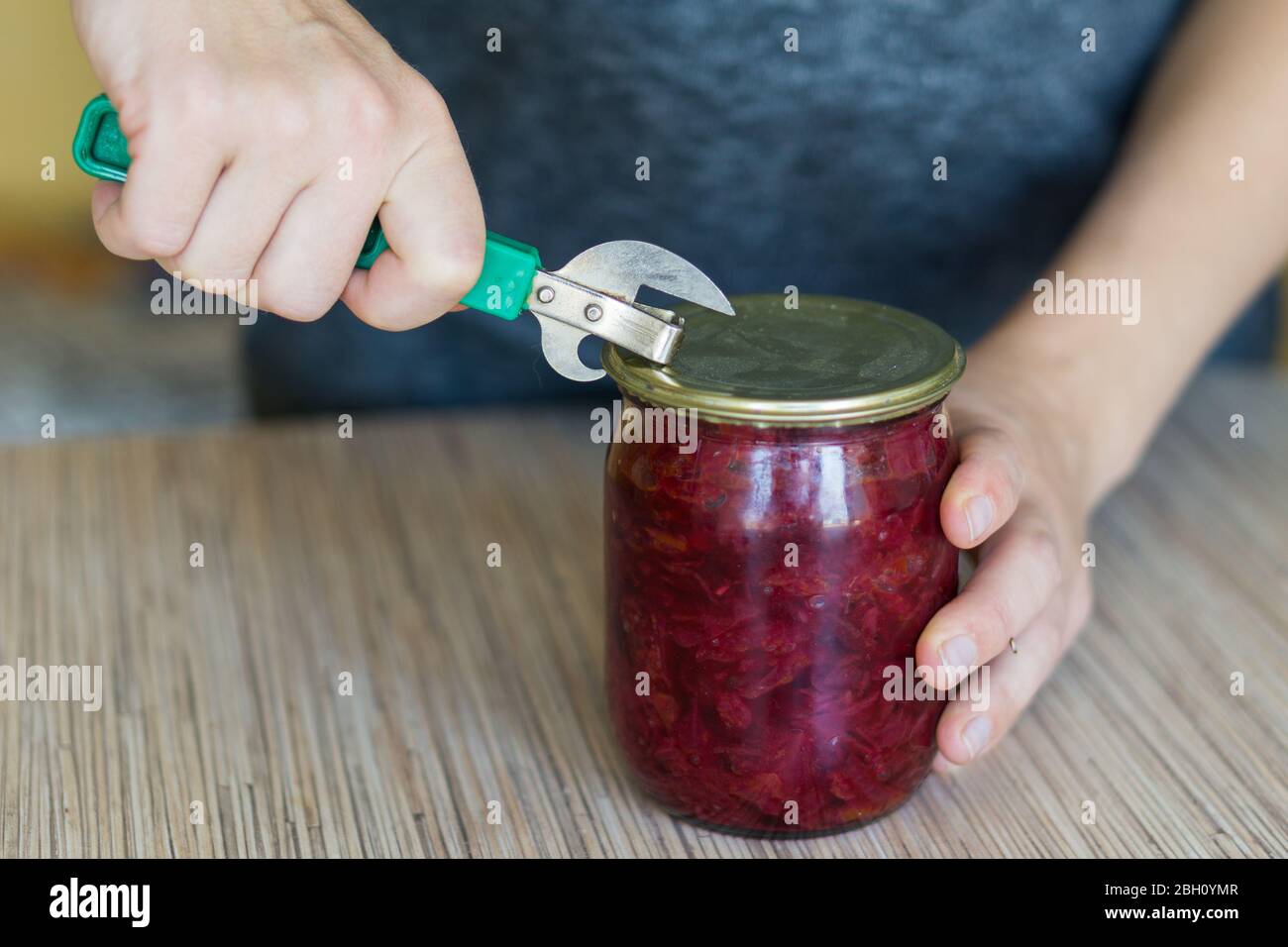 Closeup of woman opening a can in a kitchen with old style tin opener. Stock Photo