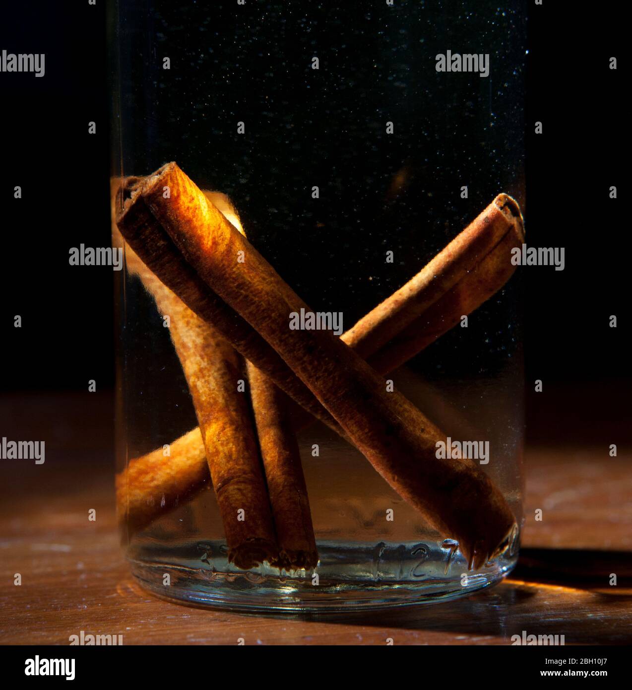 Cinnamon sticks sit in a glass bottle of vodka to make homemade infused flavored vodka Stock Photo