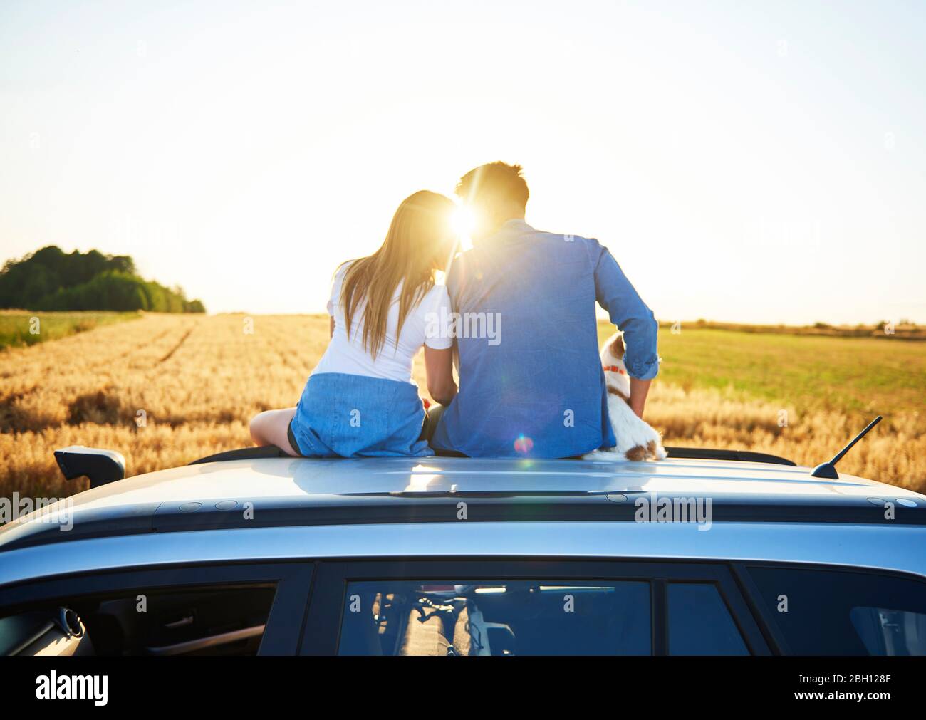 Rear view of loving couple embracing and sitting on car Stock Photo