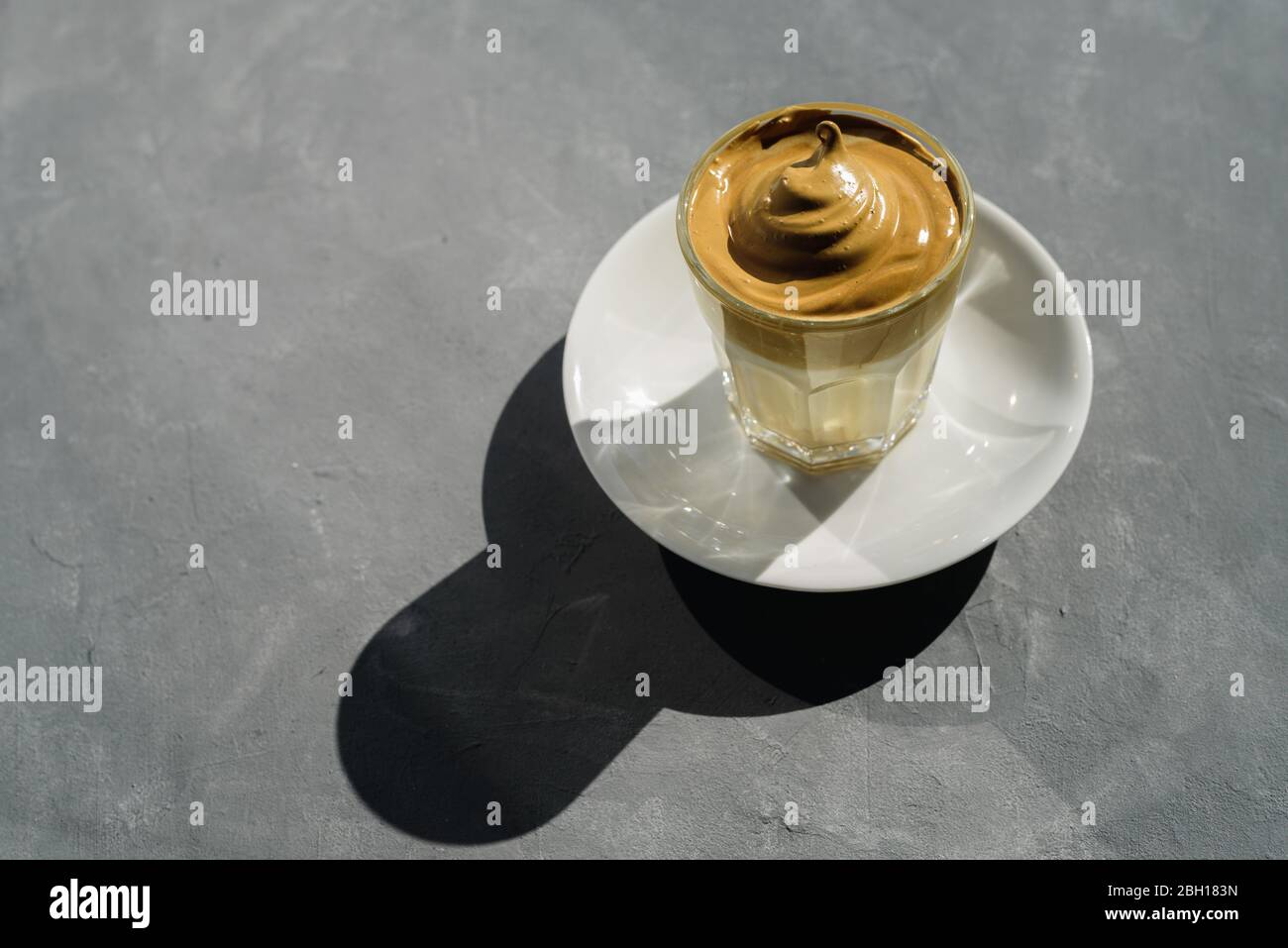 Dalgona instant coffee whipped drink in glass with plate. Hard sun