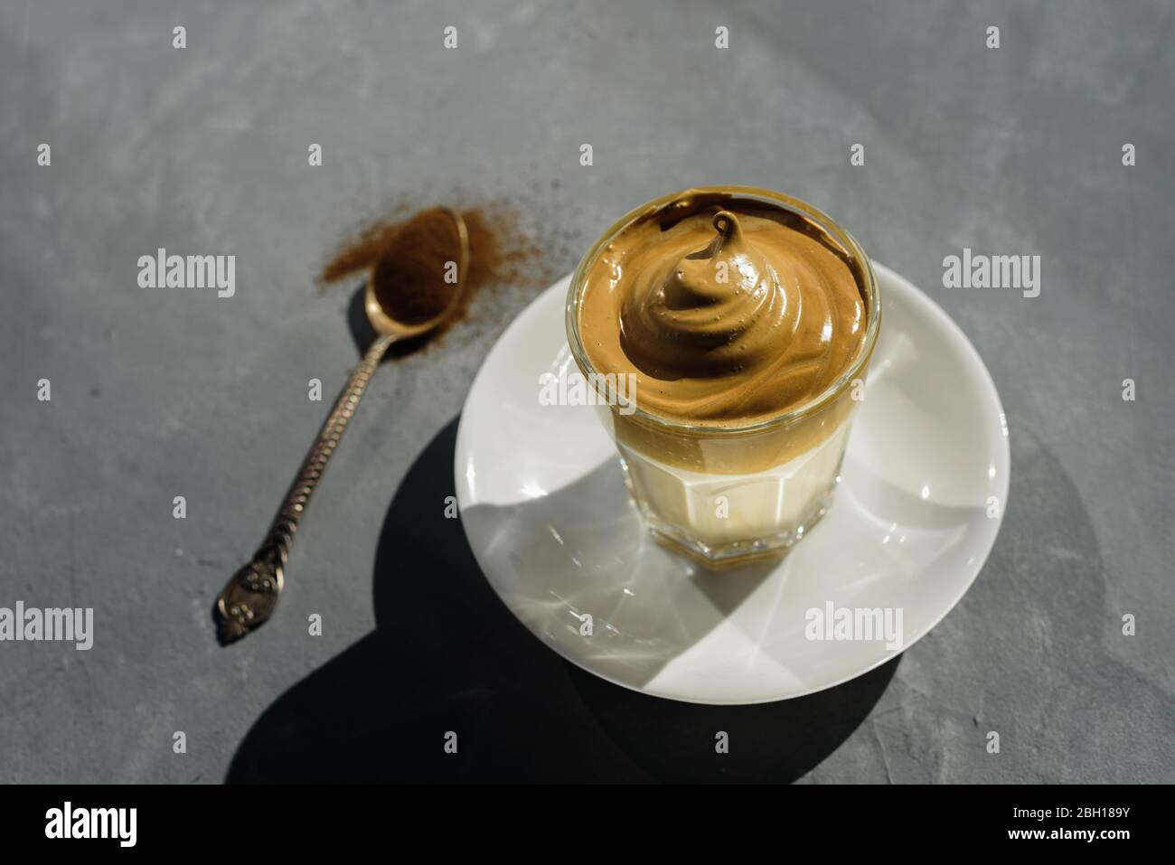 Dalgona instant coffee whipped drink in glass. Hard sun light, concrete