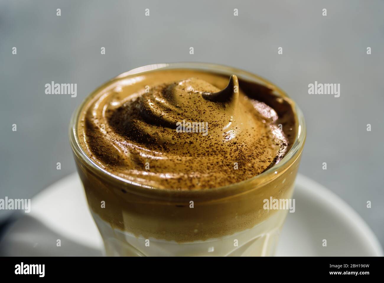 Dalgona instant coffee whipped drink in glass. Hard sun light, concrete