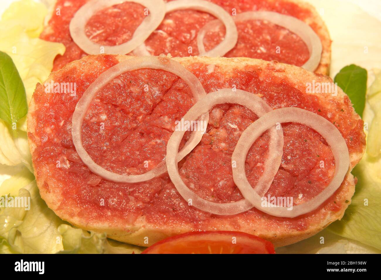 two half Mett on bread rolls with onion rings on lettuce, Germany Stock Photo
