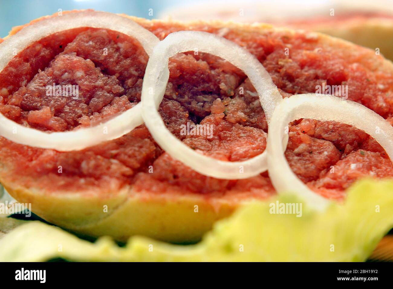 half Mett on bread roll with onion rings on lettuce, Germany Stock Photo
