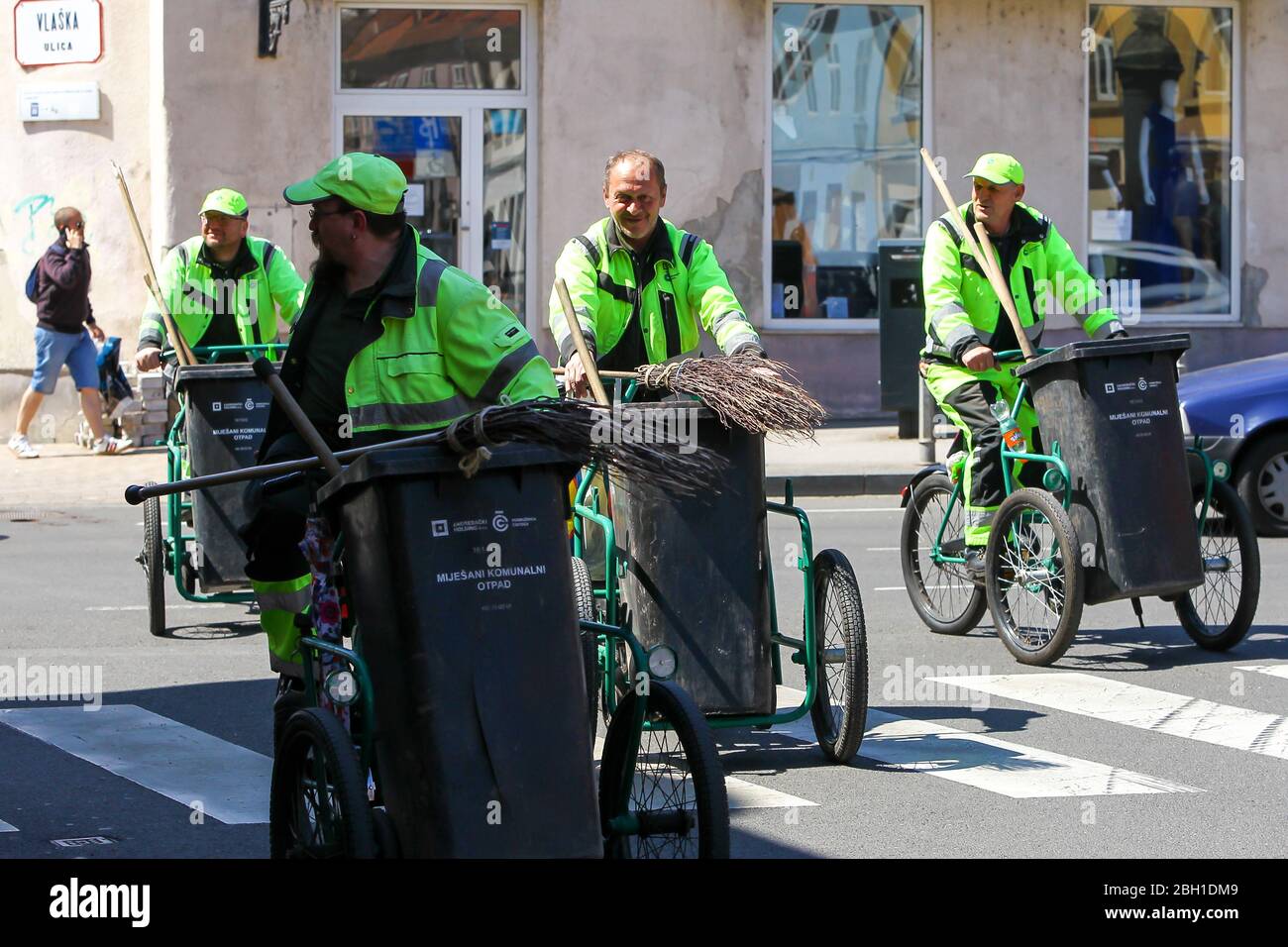 Zagreb, Croatia - April 17, 2020 : A group of garbage man driving bikes with trash cans on it in downtown of Zagreb, Croatia. Stock Photo