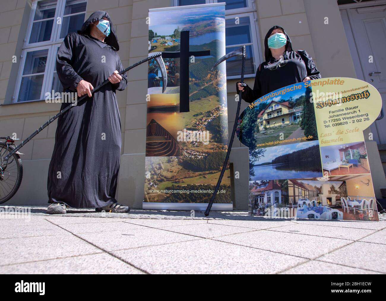 Schwerin, Germany. 23rd Apr, 2020. Members of tourism enterprises demonstrate their hands for financial aid and tax relief to save the closed enterprises, while observing the corona protection measures and using imitation scythes. The Hotel Community Müritz is an association of 19 small, owner-operated hotels with 633 beds. Credit: Jens Büttner/dpa-Zentralbild/dpa/Alamy Live News Stock Photo