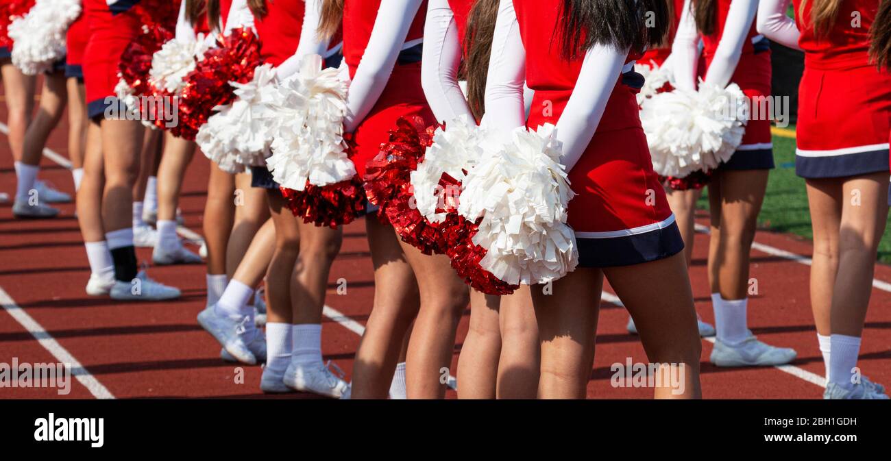 High school cheerleader with their pom poms behind their back whatching the football game they are cheering at. Stock Photo