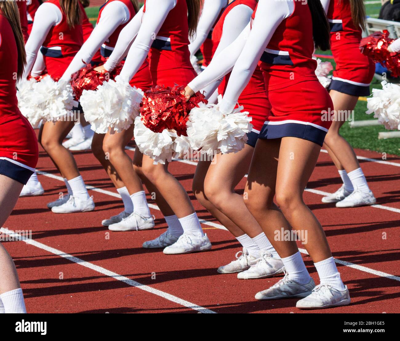 High school cheerleaders standing on a red track performing a routine with red and white pom poms. Stock Photo