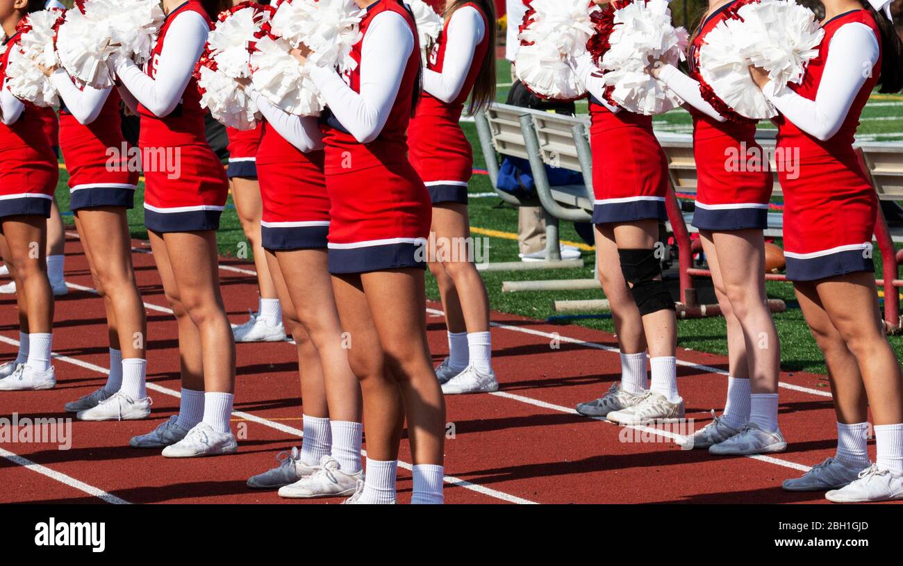 High school cheerleaders in red and white uniforms cheer for the fans at a high school football game. Stock Photo