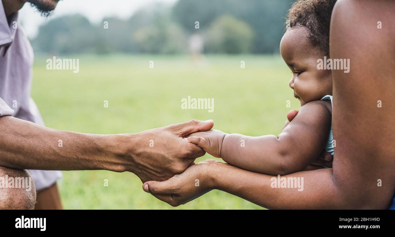 Happy african family holdings hands together outdoor during mother day - Mom, father and daughter having tender moments in nature green park - Love an Stock Photo