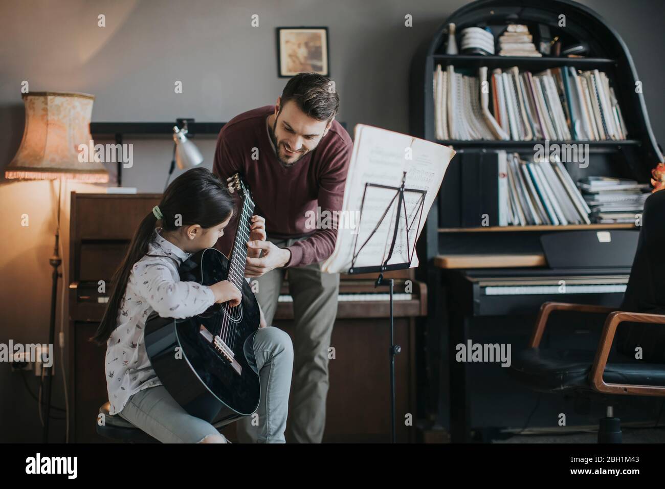 Cute little girl playing guitar with her music teacher in the rustic