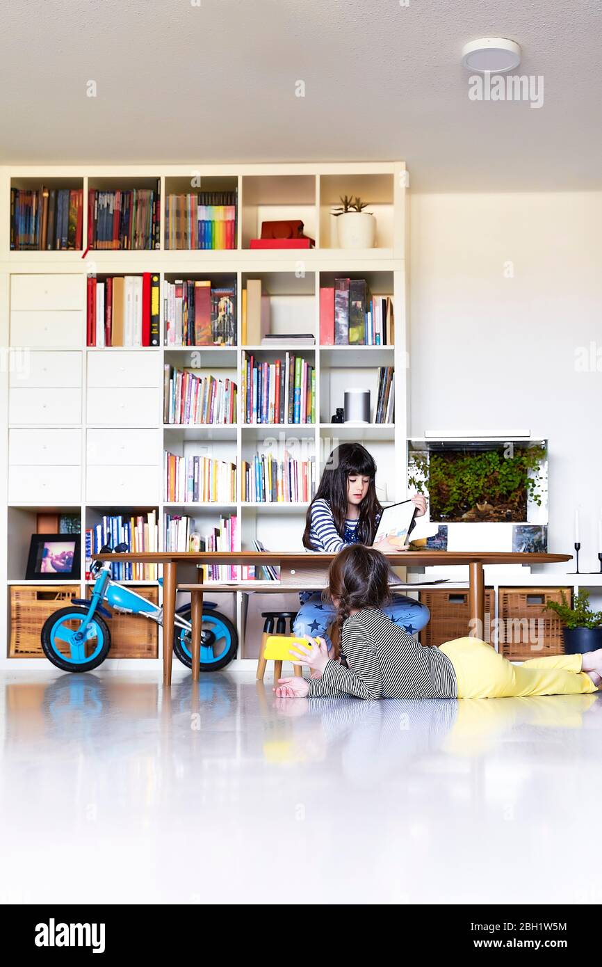 Sisters using electronic devices at home Stock Photo