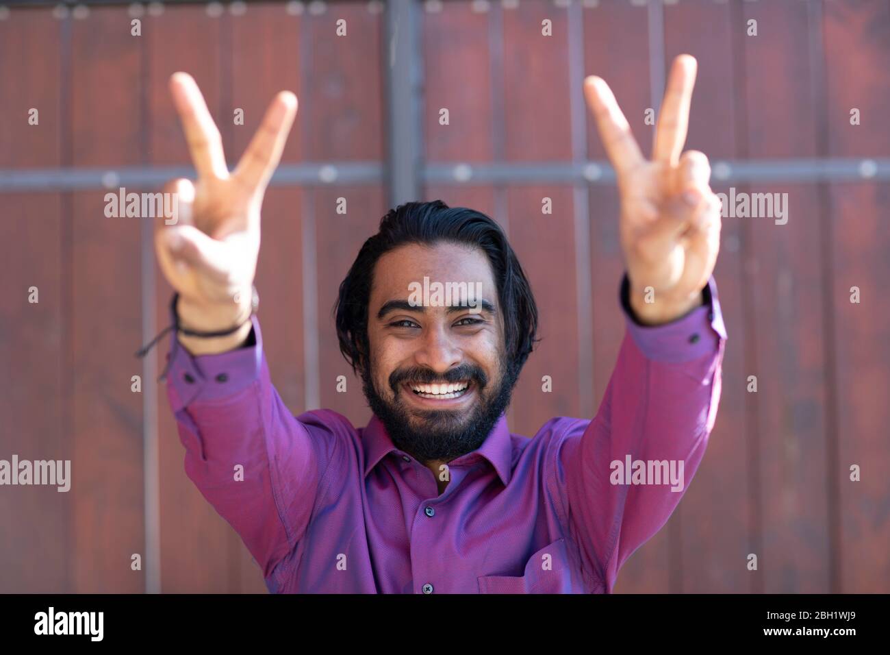 Young smiling man making peace sign in front of a gate Stock Photo
