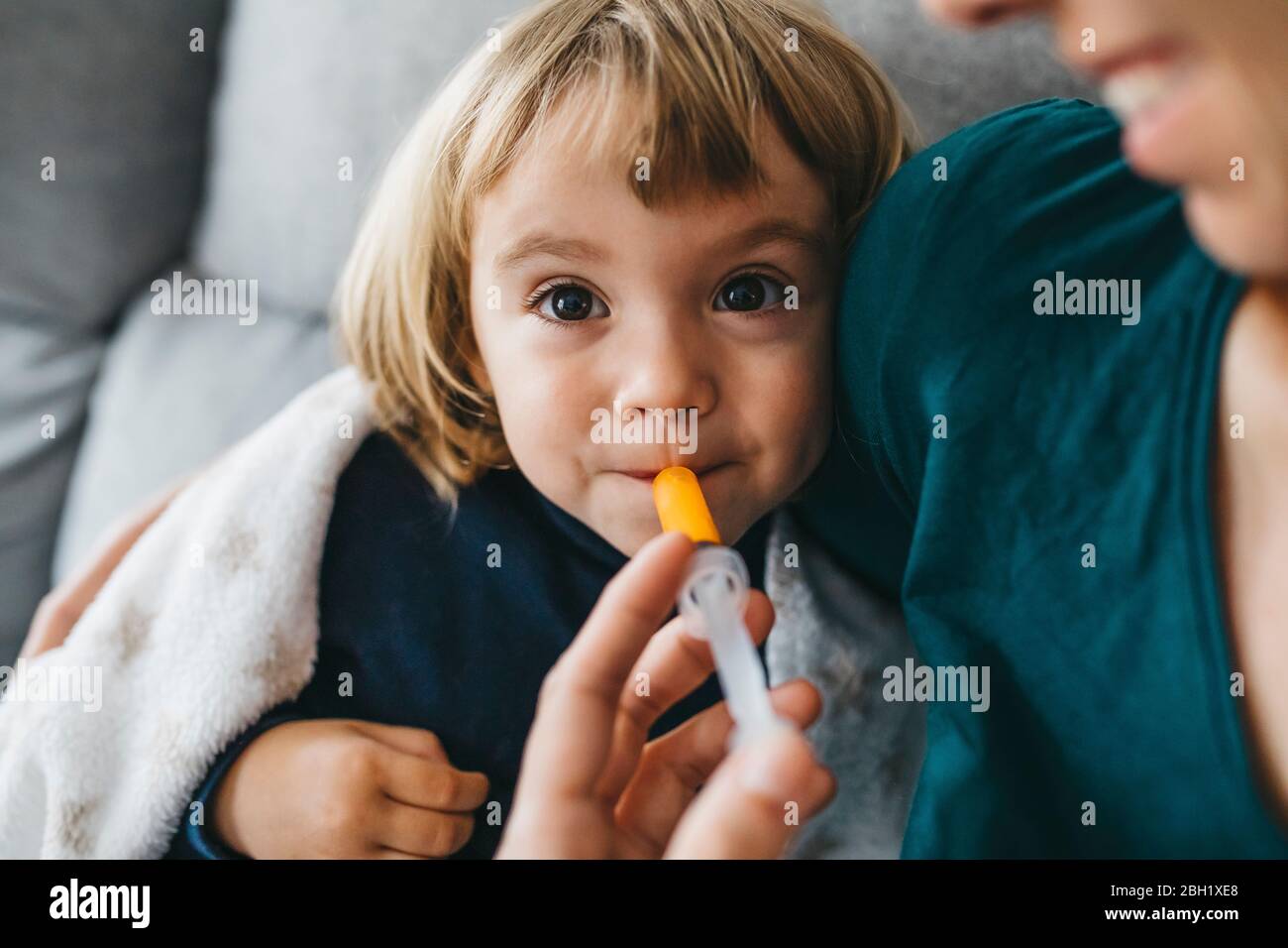 Portrait of sick little girl sitting on couch while mother giving her medication Stock Photo