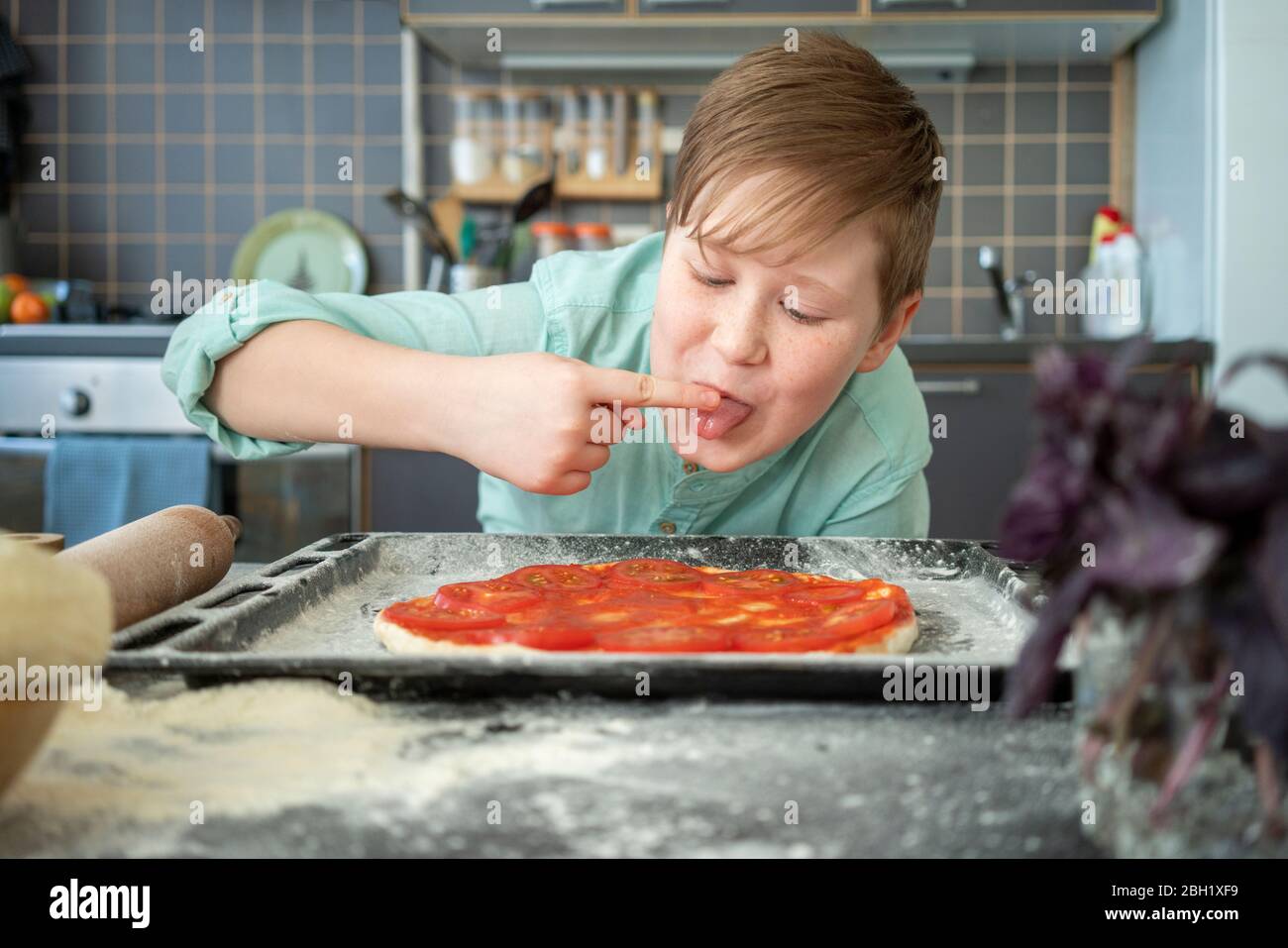 Portrait of boy nibbling tomato sauce in kitchen Stock Photo