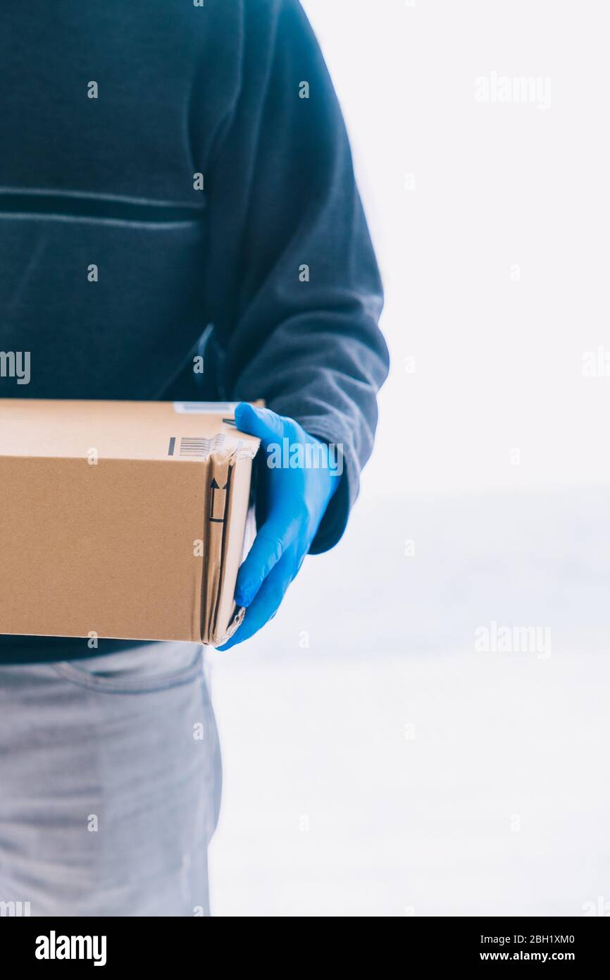 Delivery person delivering a package with blue latex gloves as a measure of protection against the coronavirus. Stock Photo