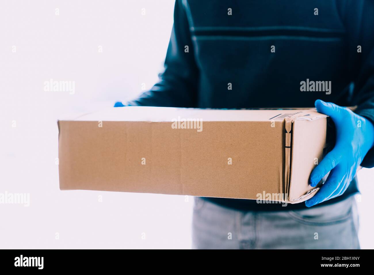 Delivery person delivering package with blue latex gloves as a safety measure for the coronavirus. Deliverers in quarantine time with copy space. Stock Photo