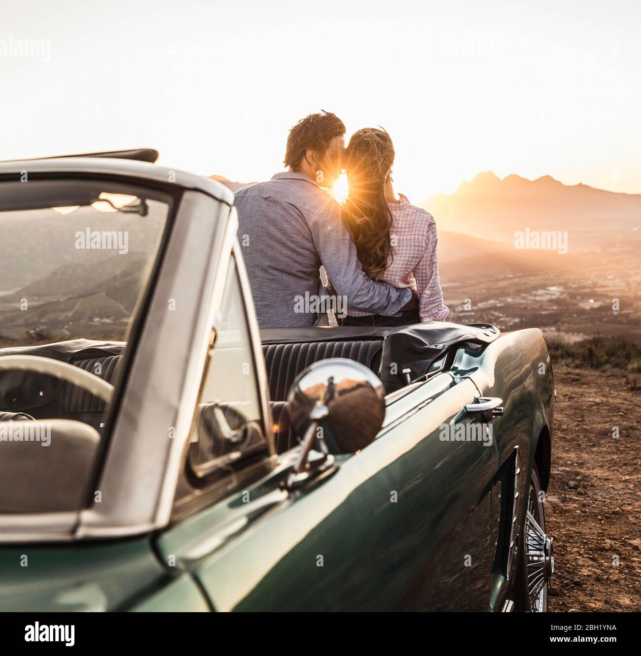 Affectionate couple at convertible car in the countryside at sunset Stock Photo