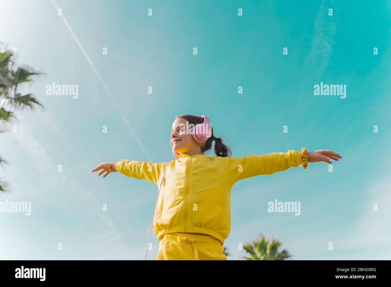 Happy little girl wearing with arms outstretched listening music with headphones outdoors Stock Photo