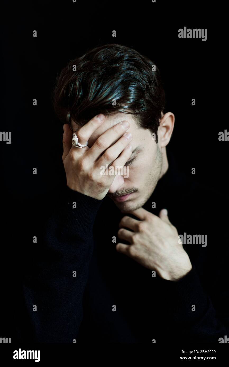 Portrait of young man with eyes closed and hand on face against black background Stock Photo