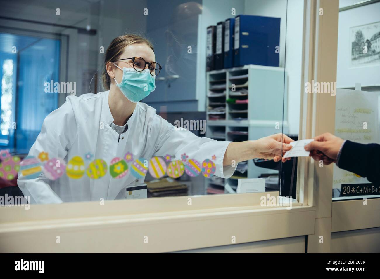 Employee at reception desk of hospital ward handing over card to visitor Stock Photo