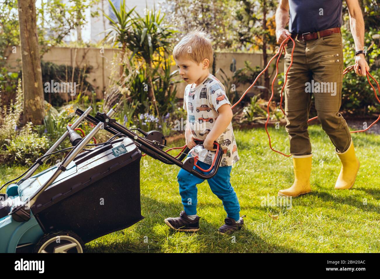 Toddler boy mowing the lawn with his father Stock Photo