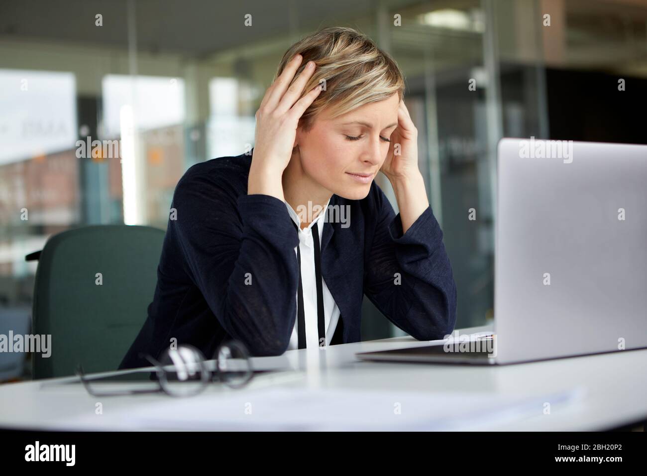 Businesswoman in office with head in hands and closed eyes Stock Photo