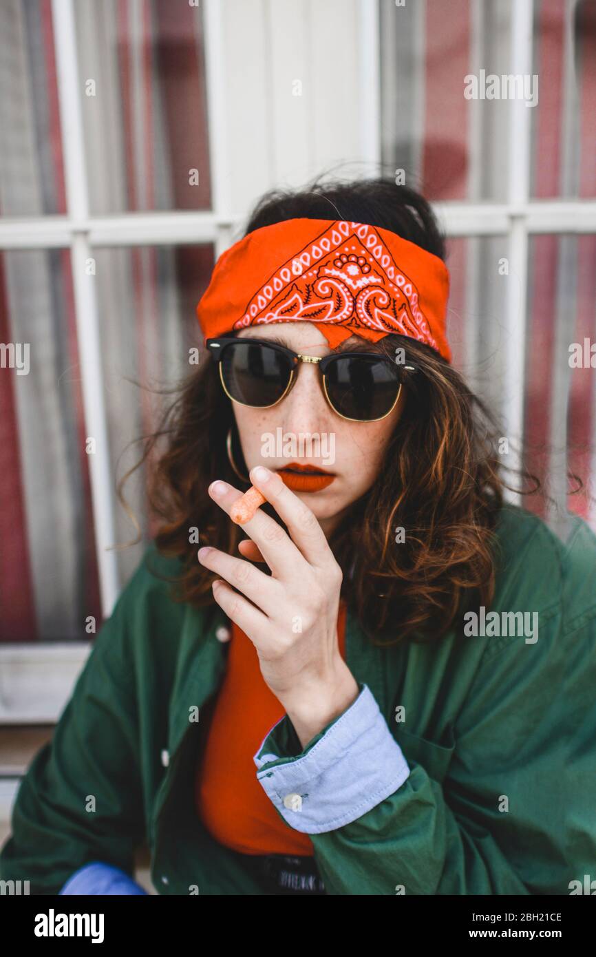 Portrait of young woman wearing headband and sunglasses smoking carrot