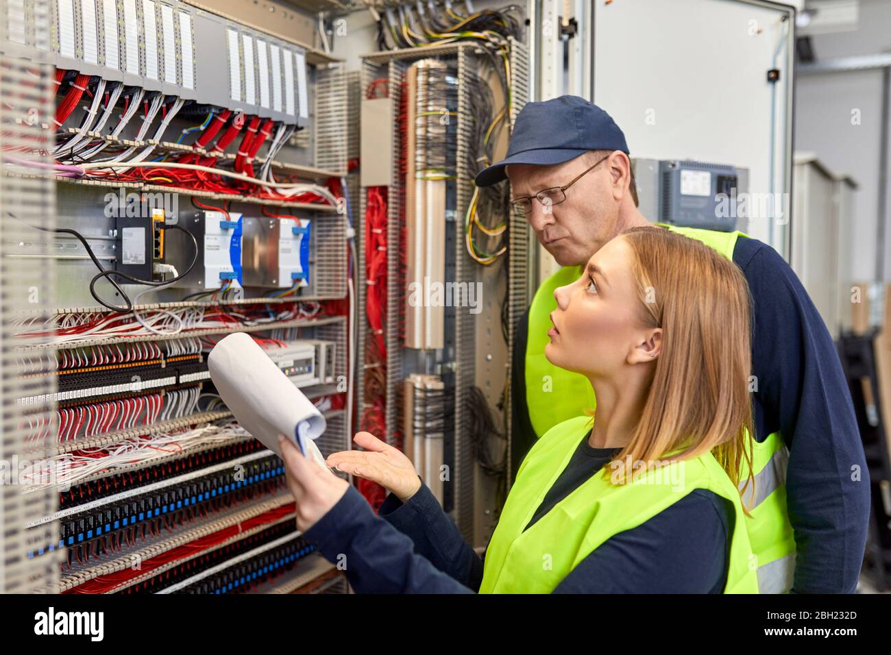 Two electricians with plan looking at fuse box Stock Photo