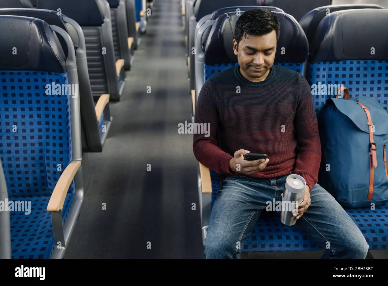 Man holding reusable cup and using smartphone in the train Stock Photo