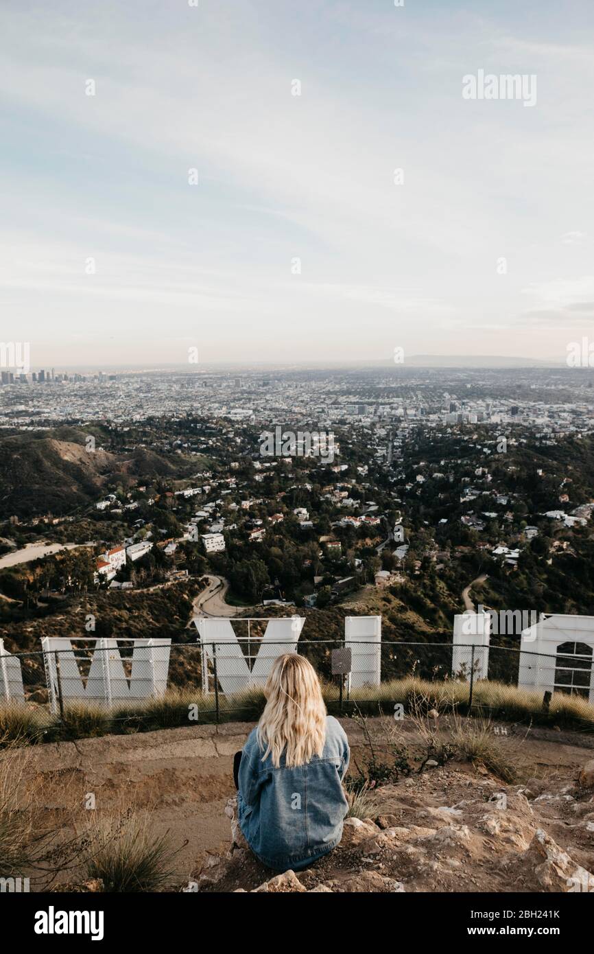 Back view of blond woman sitting behind Hollywood sign looking at view, Beverly Hills, USA Stock Photo