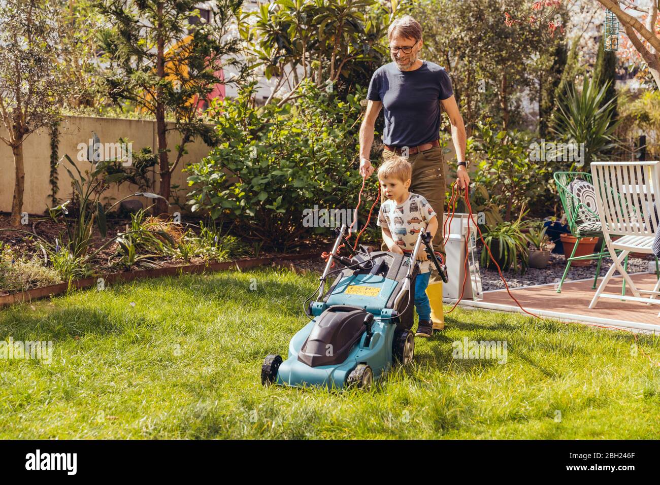 Father and son mowing the lawn together Stock Photo