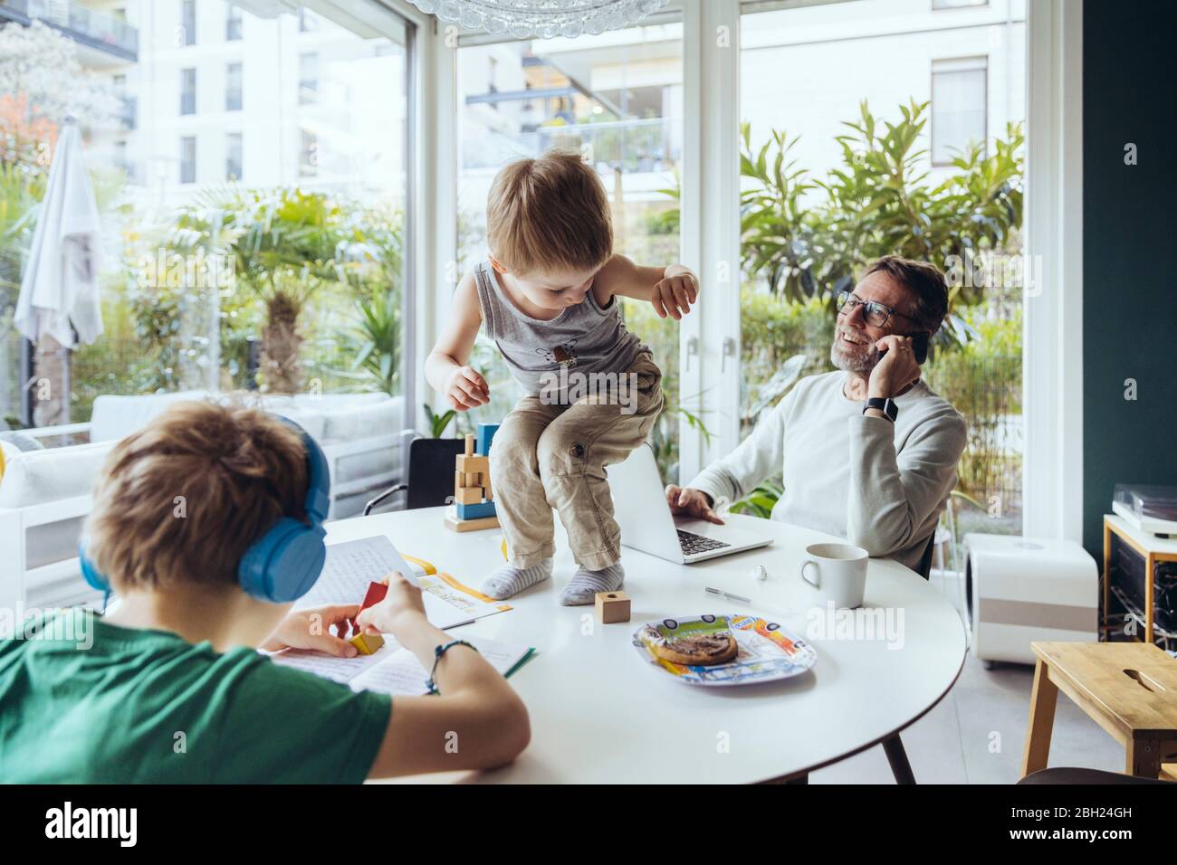 Father talking on the phone while sons are playing on the table Stock Photo