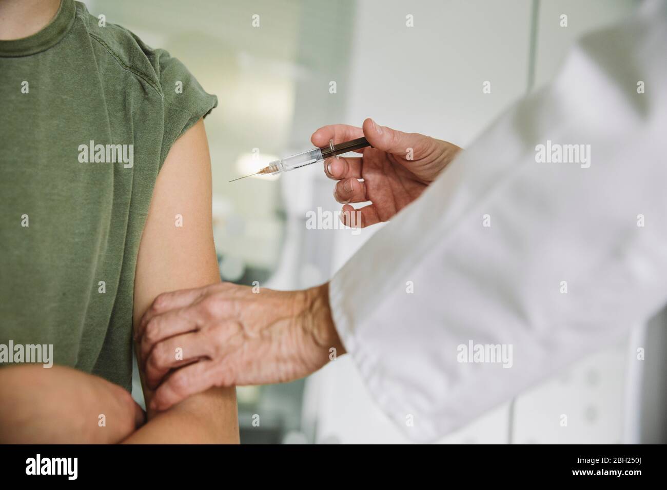 Doctor injecting vaccine into arm of teenager Stock Photo