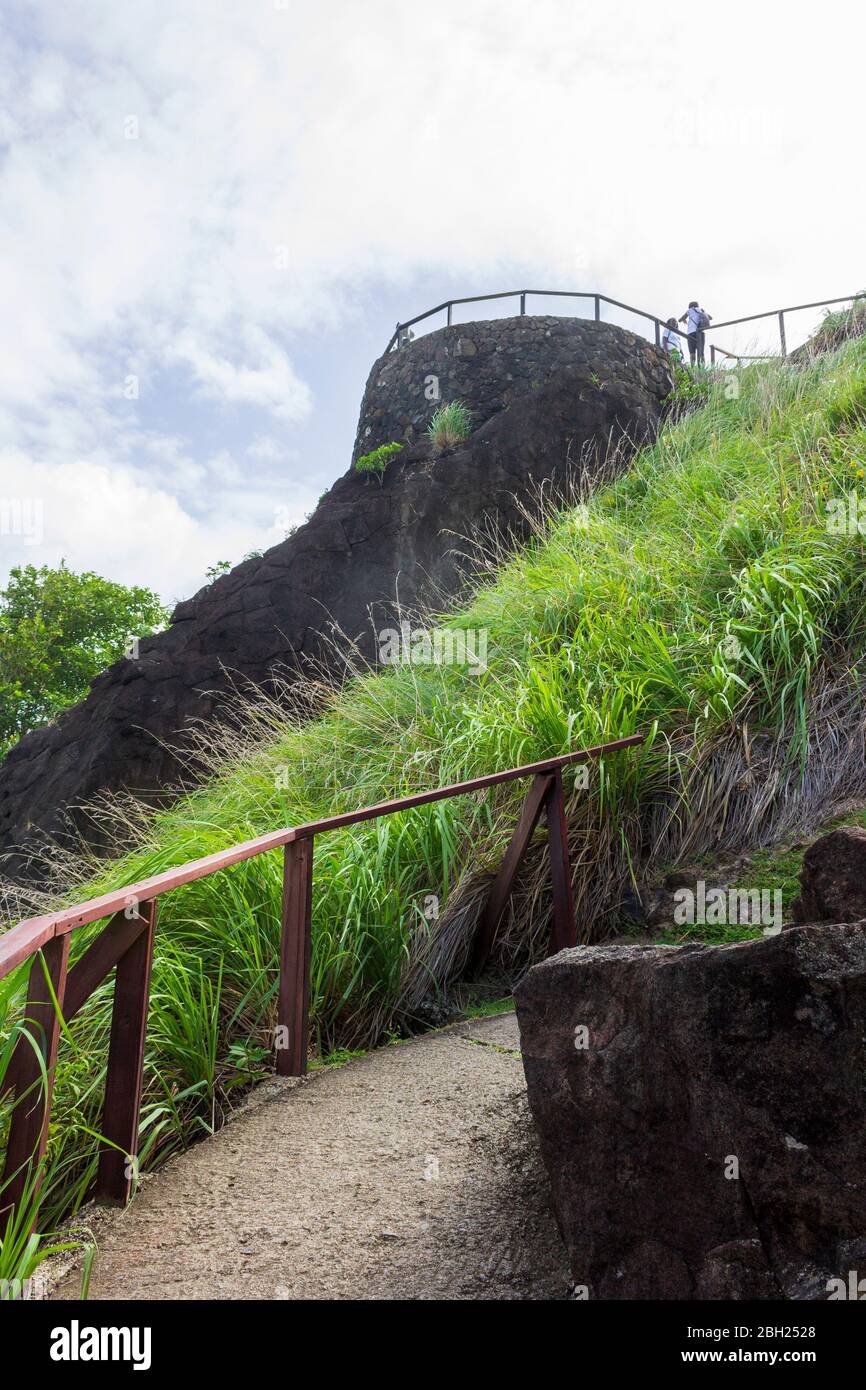 Breathtaking view of the concrete pathway with a wooden handrail with green grass and trees on either side leading up to the top of Fort Rodney Stock Photo