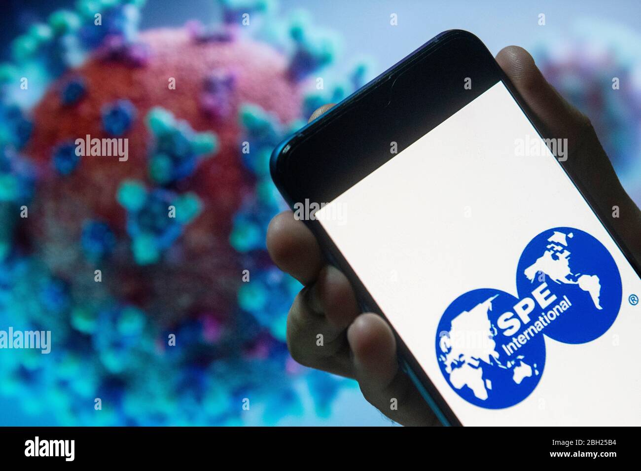 In this photo illustration a Society of Petroleum Engineers (SPE) logo seen displayed on a smartphone with a COVID-19 coronavirus image in the background. Stock Photo